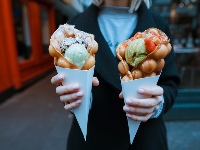 Eine Dame hält zwei Bubble Waffles mit Eis und Topping