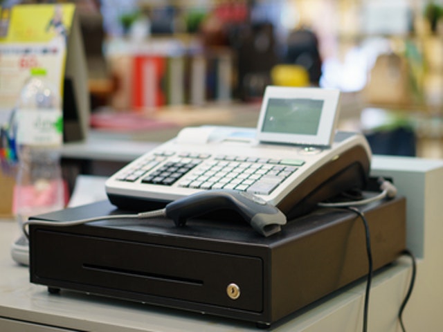 Auf dem Bild ist eine einfache Registrierkasse mit Geldschublade und Handscanner zu sehen